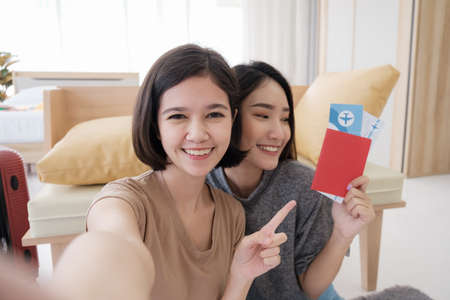 Two young Asian women are selfie with smartphones and showing flights and passport them while planning a summer trip in their bedroom.concept of travel in summer and holiday.の写真素材