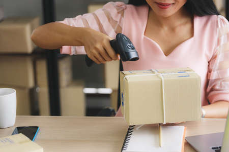 Asian businesswoman start-up online seller owner using computer for checking the customer orders from email or website and preparing packages - online shopping or sell online conceptの写真素材