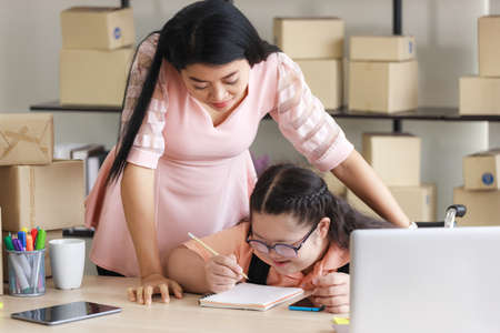 Middle-aged mother and an autistic Asian daughter prepare products for delivery to customers in a home converted to a small business office online. New business in the era of the COVID-19 epidemic.の写真素材