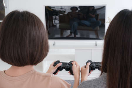 Two Asian girlfriends enjoy playing video games with joysticks at home. Lesbian couples or lgbt activities on vacation inside the room.の写真素材