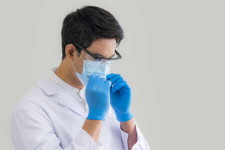 Close up male doctor, researcher, scientist wearing eye protection glasses, white suit, glove and mask on grey background. Healthcare and medical concept.の写真素材