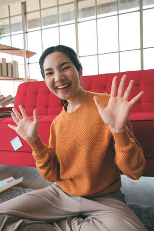 Young Asian woman was a video call and waving her hand through the application from smartphone to study online, work from home, and transact online during the outbreak.の写真素材