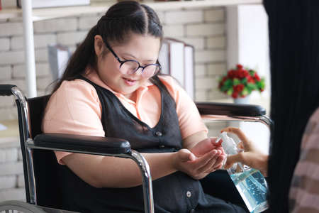 A mother teaches an Asian autistic girl who sits in a wheelchair e to wash his hands with alcohol gel in the epidemicの写真素材
