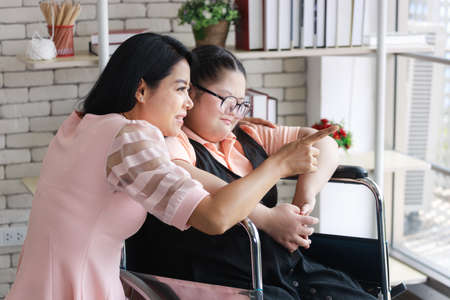 Asian mother with young girl on wheelchair in a room at home, mother pointing outside the windowの写真素材