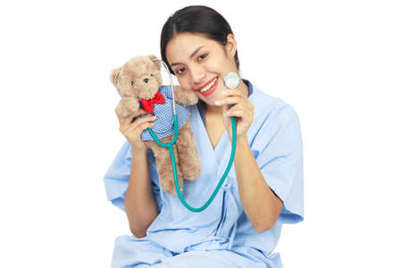 Isolated friendly young doctor smiling and holding a teddy bear with stethoscope on white background. Healthcare and medical concept.の写真素材