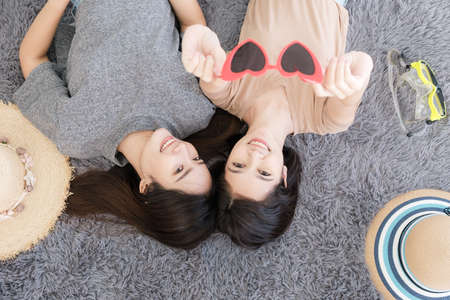 Portrait of two young Asian women show sunglasses in summer concept smiling and lying on the white floor to selfy take a photo.の写真素材