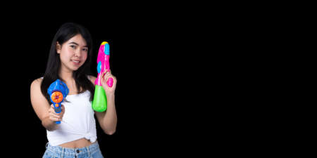 Portrait cheerful young Asian woman holding water gun Smiling and having fun playing in the water Songkran festival, Thailand. isolated on black background. Thai New Year's Day.の写真素材