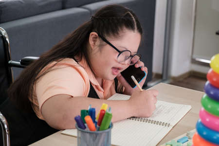 Lovely Asian girl is writing and talking on the phone with her teacher regarding her homeworkの写真素材