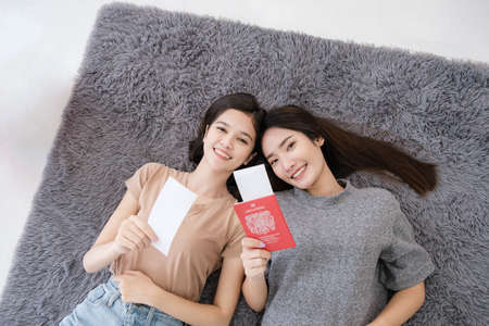 Two young Asian women are planning their summer vacation and are preparing their plane tickets, passports, maps, and clothes in their bedroom. concept of travel in summer and holiday.の写真素材
