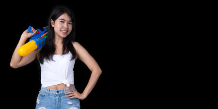 Portrait cheerful young Asian woman holding water gun Smiling and having fun playing in the water Songkran festival, Thailand. isolated on black background. Thai New Year's Day.の写真素材