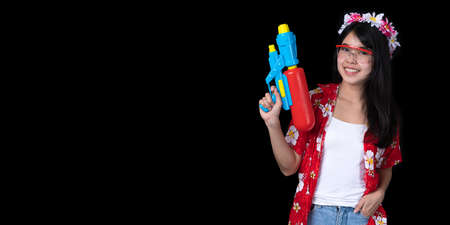 Portrait cheerful young Asian woman holding water gun Smiling and having fun playing in the water Songkran festival, Thailand. isolated on black background. Thai New Year's Day.の写真素材