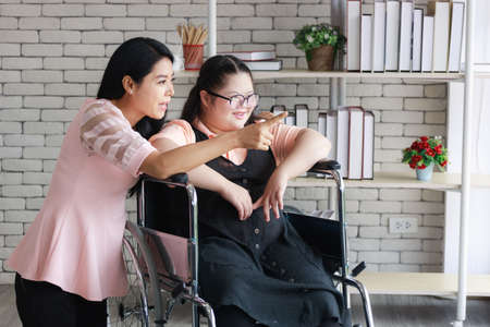 Asian mother with young girl on wheelchair in room at home.の写真素材