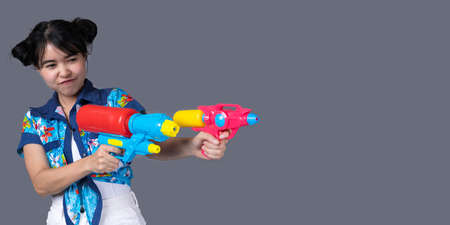 Portrait cheerful young Asian woman holding water gun Smiling and having fun playing in the water Songkran festival, Thailand. isolated on grey background. Thai New Year's Day.の写真素材