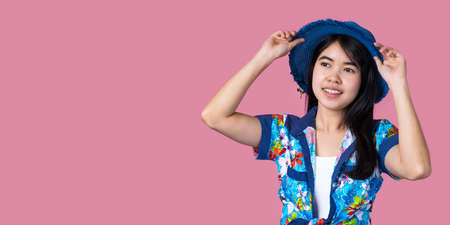 Portrait of a beautiful Asian woman wearing a blue hat and a Hawaiian shirt with a pink background Summer conceptの写真素材