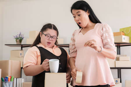 Middle-aged mother with an autistic Asian daughter is thrilled as she wraps products for delivery to customers in a home converted to a small business office online. New business in the era of the COVID-19 epidemic.の写真素材