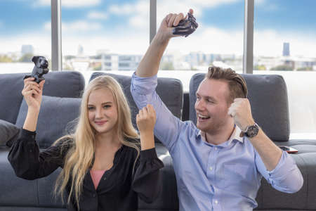 Young couple sitting on the floor at home. Portrait of wife and husband have fun playing video games with a joystick. stay at home.の写真素材