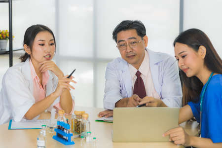 Three people of team of medical personnel, consisting of a senior male doctor, a young female doctor, and a young nurse with laptop are meeting in a meeting room in the hospital.の写真素材