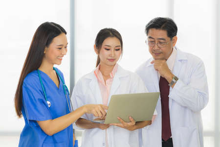 Three people of team of medical personnel, consisting of a senior male doctor, a young female doctor, and a young nurse with laptop are meeting in a meeting room in the hospital.の写真素材