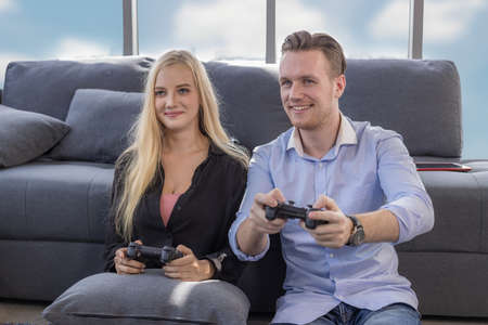 Young couple sitting on the floor at home. Portrait of wife and husband have fun playing video games...