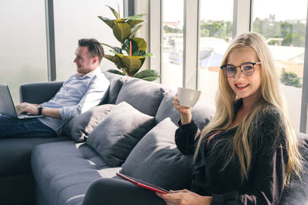 Portrait of woman drinking coffee and using a tablet for communication and searching information online. Young businesswoman working from home.の写真素材