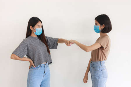 Two asian teenage girls wearing mask and greeting each other using punch.の写真素材