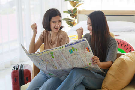 Two young Asian women are looking at maps to plan a summer trip on the sofa in their bedroom. concept of travel in summer and holiday.の写真素材