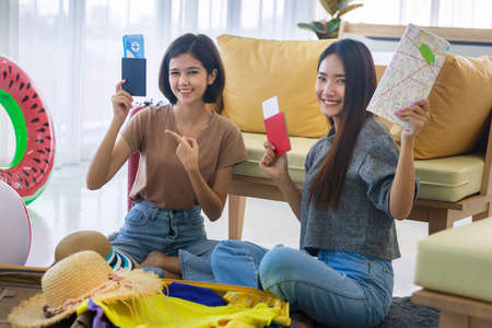 Two young Asian women are planning their summer vacation and are preparing their plane tickets, passports, maps and clothes in their bedroom. concept of travel in summer and holiday.の写真素材