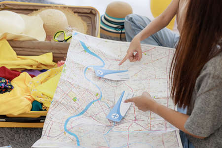 Two young Asian women are planning their summer vacation and are preparing their plane tickets, passports, maps and clothes in their bedroom. concept of travel in summer and holiday.の写真素材
