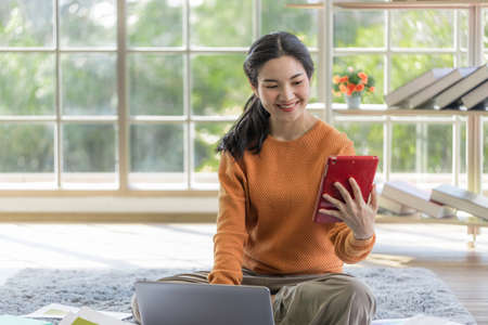young Asian woman relaxing on the floor inside the house. Young women use tablet to entertainment...