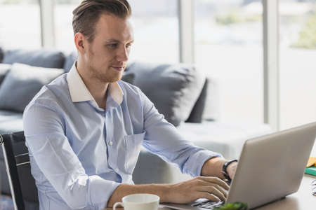 Portrait of young man working from home-office with morning sunshine. happy man communicating in social network and searching information online.の写真素材