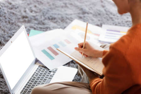 A young Asian business woman sits at home using a laptop computer operated by a video conferencing...