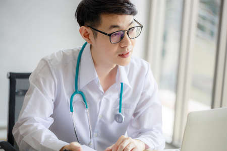 Young Asian male doctor is recording a medical history on the clipboard and explaining something to the female patient. Medical and health care conceptsの写真素材