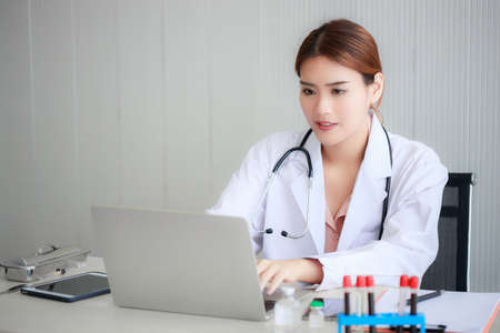 Beautiful young Asian doctor is smiling and using laptop for medical work in modern hospitalの写真素材