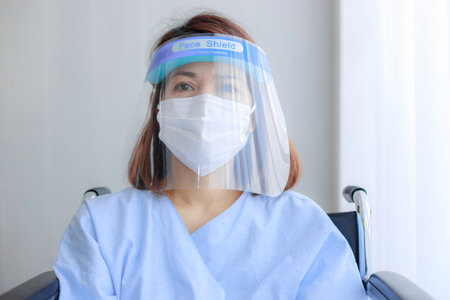 Close up Asian female patients wearing patient clothes with mask and face shield on wheelchair.の写真素材