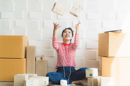 Asian freelance woman working at home and start up small business entrepreneur SME with internet online. Woman is receiving the packaging box falling from the top.の写真素材