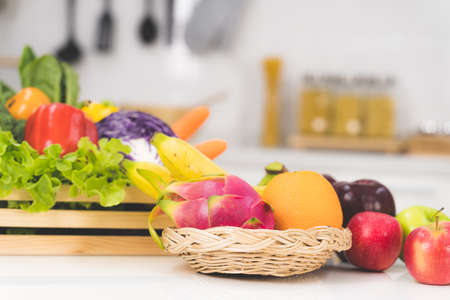 One glass of orange juice and a slice of orange with many vegetables and fruits on a white table in the kitchenの写真素材