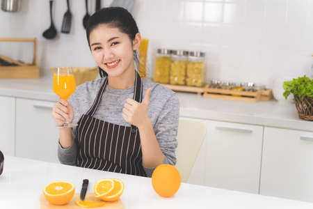 Portrait of beautiful asian woman, housewife with orange juice in white kitchen with plenty of fresh vegetables and fruits on the table.の写真素材