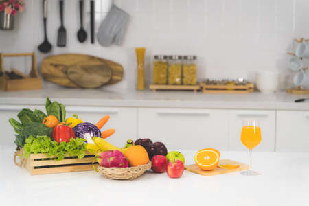 One glass of orange juice and a slice of orange with many vegetables and fruits on a white table in the kitchenの写真素材