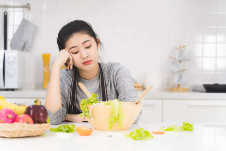 Young woman or housewife is bored of cooking, which consists of a variety of fruits and vegetables for the family.の写真素材