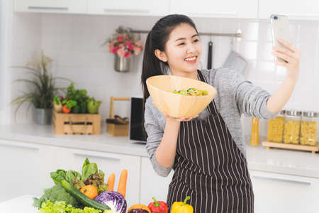 Asian young housewife, blogger is taking a selfie with a bowl of salad that she is doing to social online.の写真素材