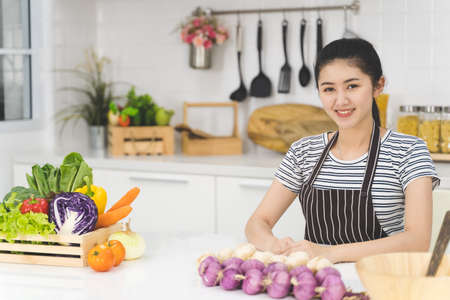 Portrait of beautiful asian woman is sitting in the bright white kitchen. wife or housewife is preparing to cook healthy food which consists of a variety of fruits and vegetables for the family.の写真素材