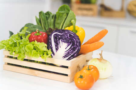 Mixing many fresh fruits and vegetables in a wooden basket placed on a white table in the kitchen.の写真素材