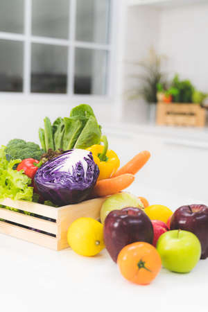 Mixing many fresh fruits and vegetables in a wooden basket placed on a white table in the kitchen.の写真素材