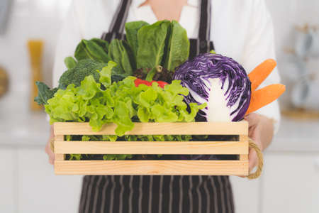 Close up wooden basket of fresh vegetables prepared for cooking, such as salad vegetables, cabbage, chilli and carrots in housewife 's hand.の写真素材