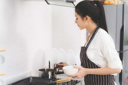 Beautiful asian woman or housewife is cooking food for family in white kitchenの写真素材
