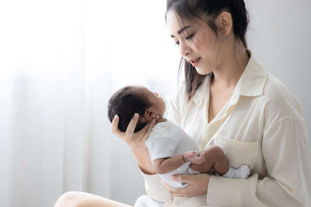 Portrait of young Asian mother happily and carrying her lovely newborn baby. Wife and mother's day concept.の写真素材
