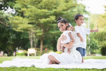 Beautiful Asian young mother  or single mom with new born baby girl and son are doing activities and relaxing in the park. concept of duties of wife and mother in raising children and family.の写真素材