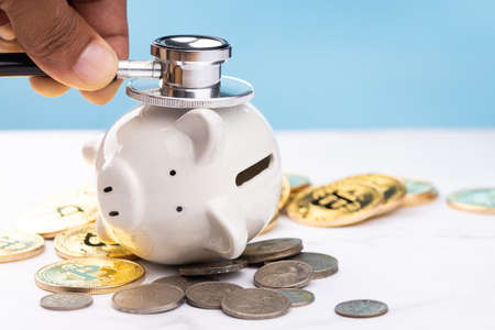 The man used stethoscope to check the piggy bank. on white table with coins and blue background. savings money concept.の写真素材