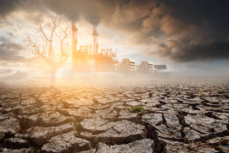 Industrial factory with lonely dead tree under dramatic evening sunset sky with cloudy drought cracked landscape. Global warming concept.の写真素材