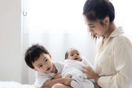 Asian young mother with cute newborn baby and the son in bed. Happy family and mother 's day concept.の写真素材